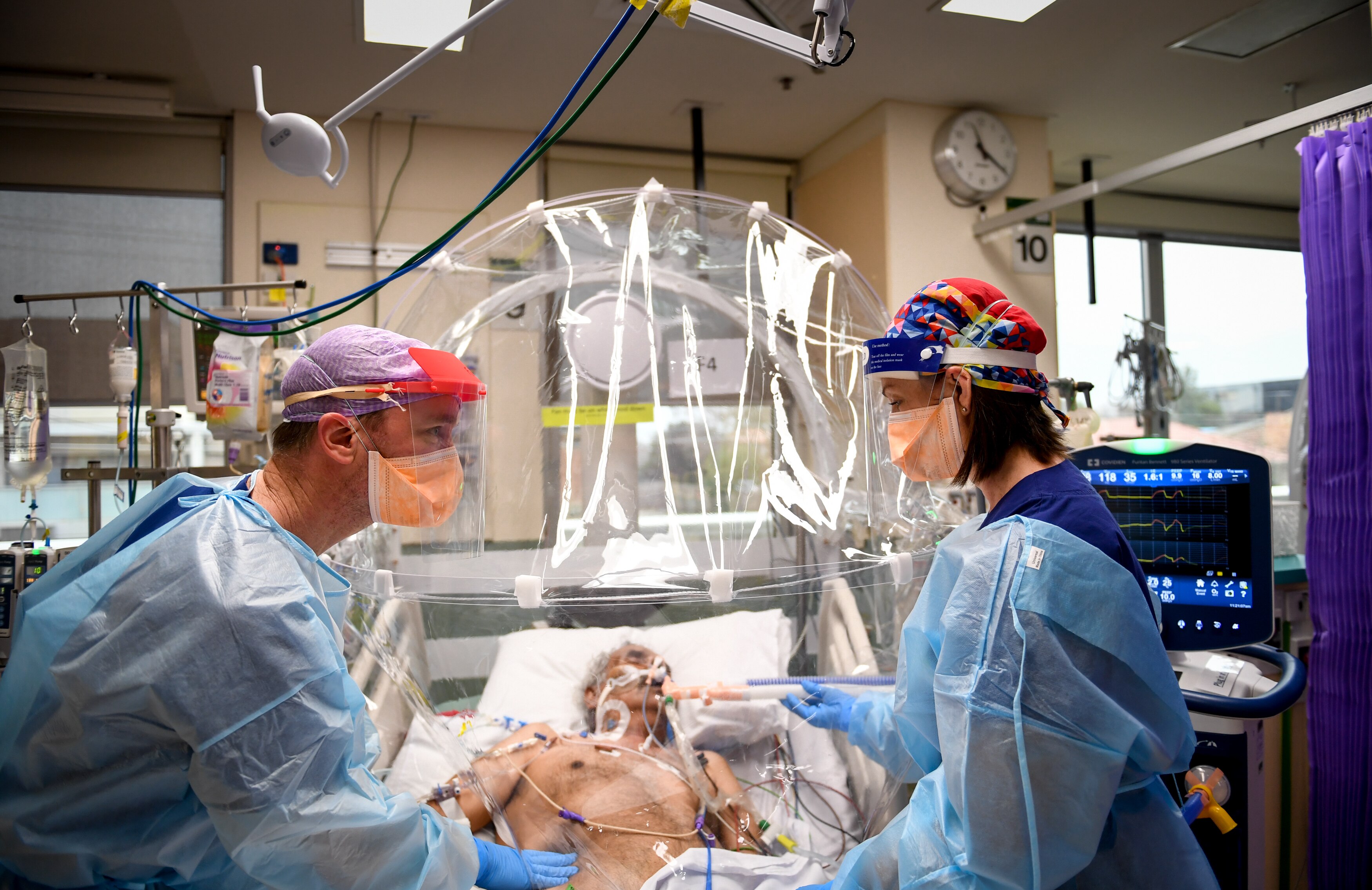 Two PPE-clad health workers tend to patient on ventilator