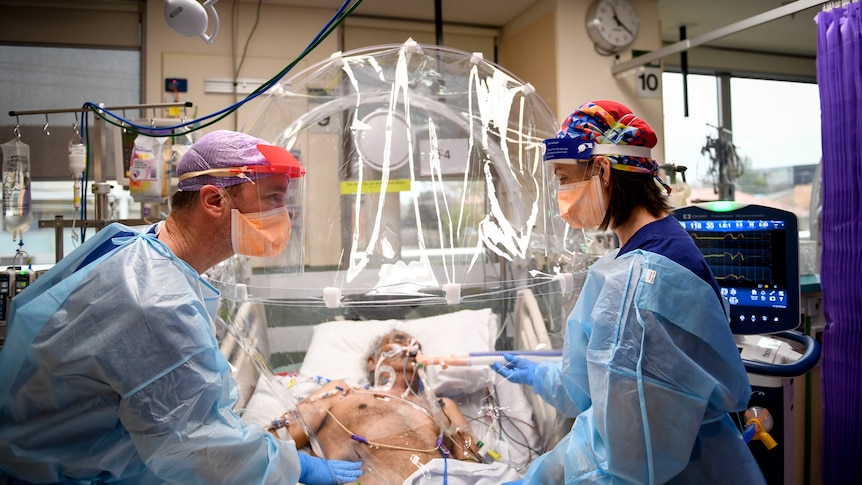 Two PPE-clad health workers tend to patient on ventilator