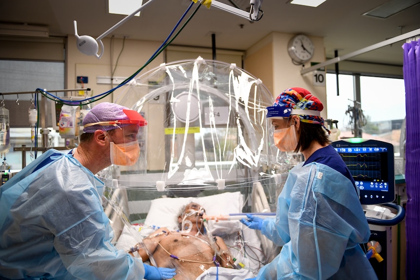 Two PPE-clad health workers tend to patient on ventilator.