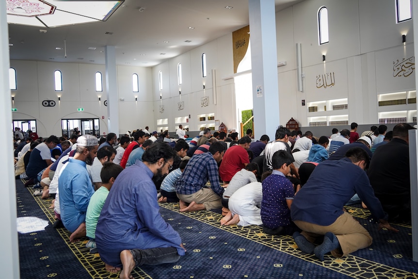 A crowd of worshippers kneel in prayer. 