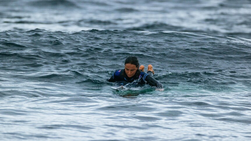A female surfer looks at the water as she paddles towards the shore
