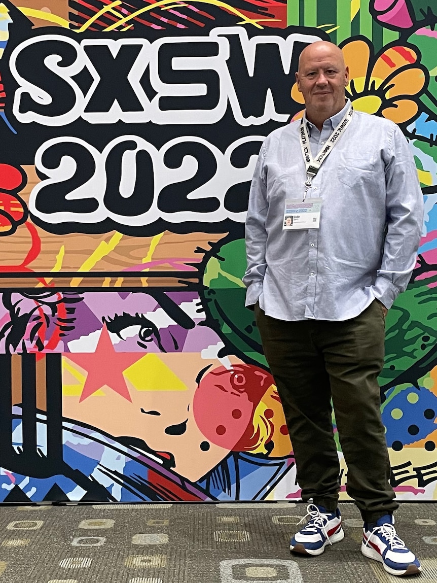 Colin Daniels dressed casually standing in front of a colourful SXSW sign
