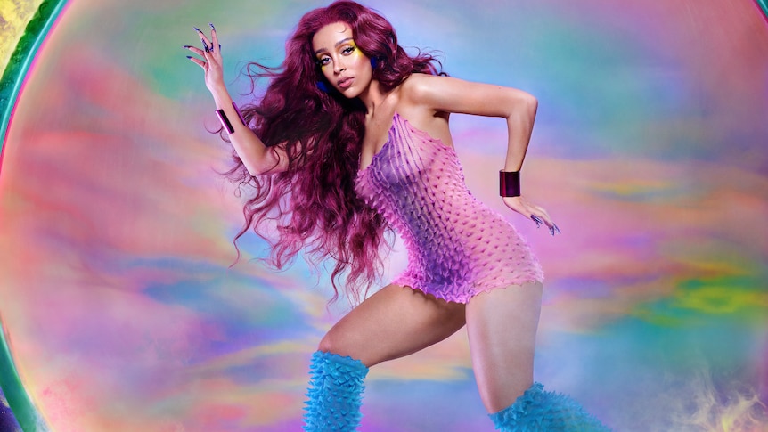 Doja Cat wearing a pink dress and knee high blue boots with hands positioned as if she's running