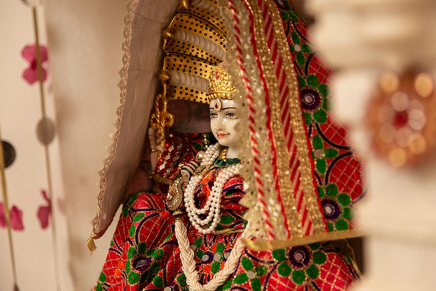 Religious idol dressed in red and gold clothing inside Jain temple.