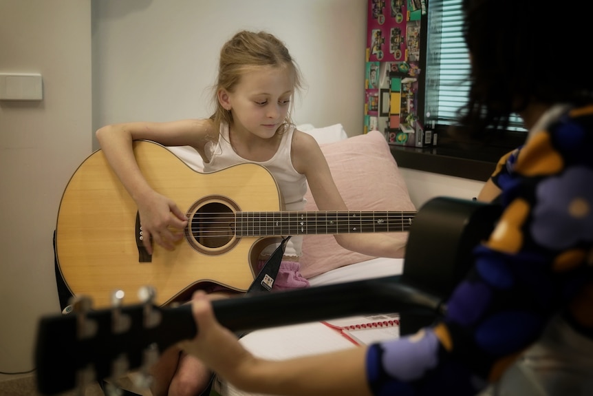 A child sits on a hospital bed holding a guitar