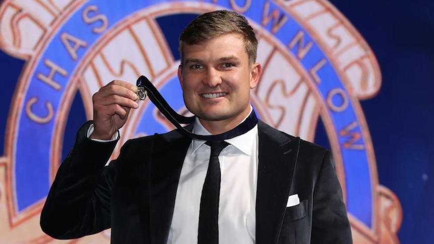 A man with blonde hair in a suit holding a small medal