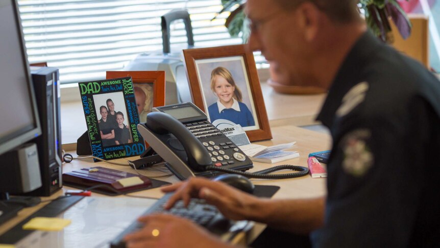 Policeman Paul Delaney works at his desk at the Toora police station, surrounded by family photos.