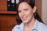 Corporate headshot of smiling woman at desk with bookshelves behind.