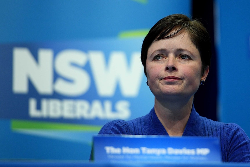 Tanya Davies looks at the camera while sitting in front of  NSW Liberal banner.