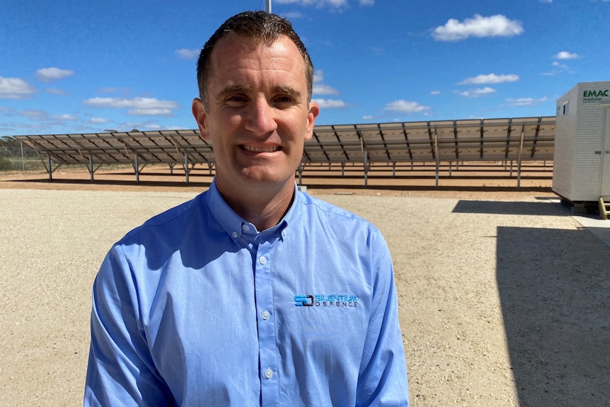 A man wearing a blue shirt standing in front of solar panels. 