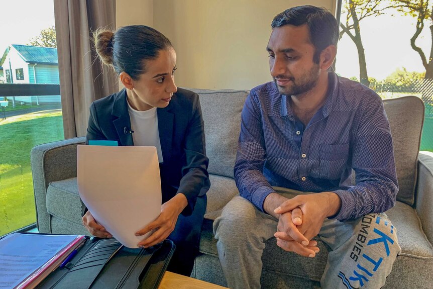 A man and a woman holding paperwork sit on a couch