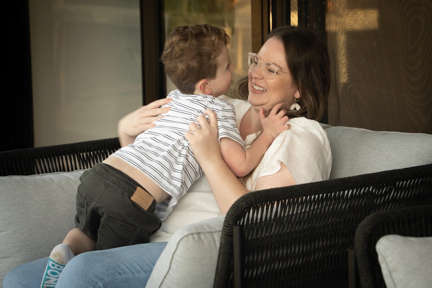 Erin Tucker sits on a cane lounge chair and smiles at Fynn who is on her lap facing her