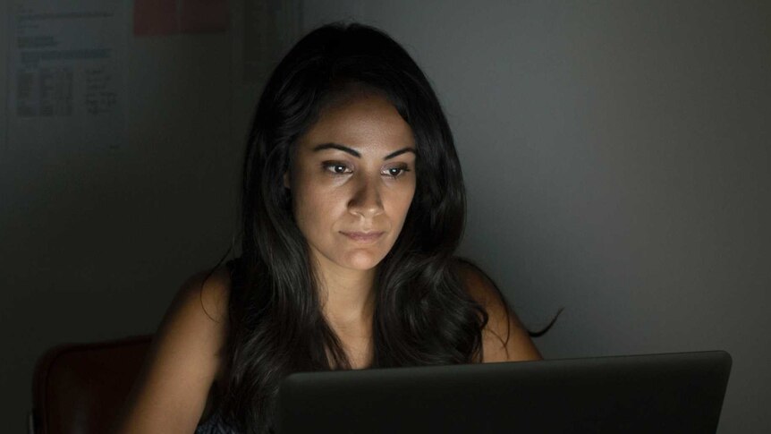 A woman sits in front of a laptop.