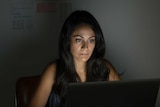 A woman sits in front of a laptop.