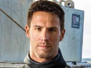 A headshot of a man with brown hair wearing a wetsuit