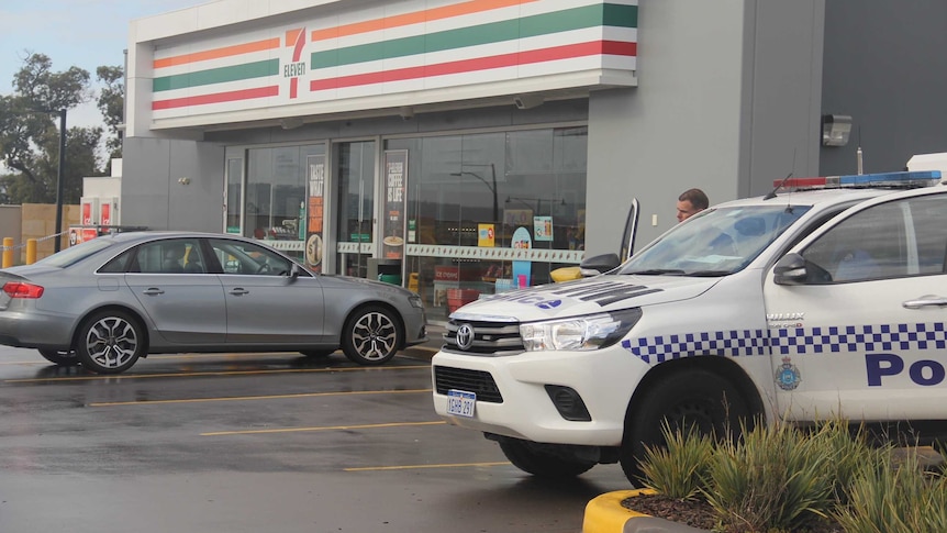 A police ute and a silver sedan sit parked outside a 7-Eleven store.