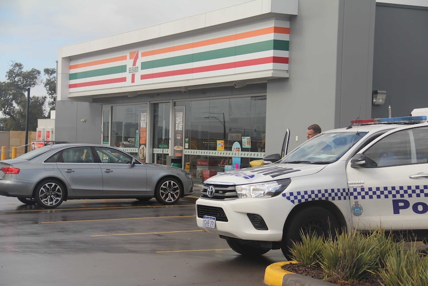 A police ute and a silver sedan sit parked outside a 7-Eleven store.