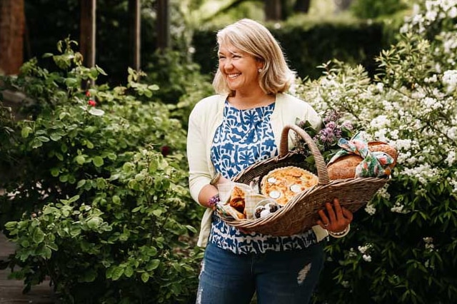 Cookbook author Sophie Hansen in a flowering garden holding a basket of baked goods.