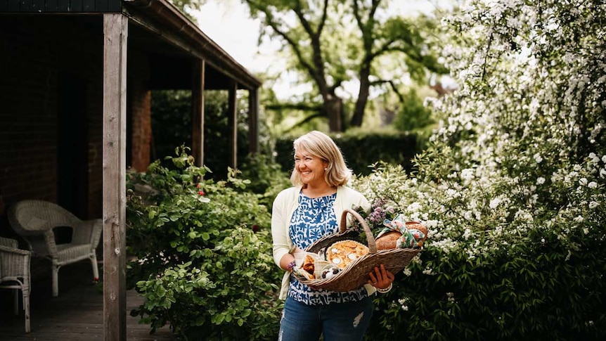 Cookbook author Sophie Hansen in a flowering garden holding a basket of baked goods.