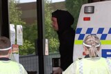 Hooded man surrounded by police in PPE.