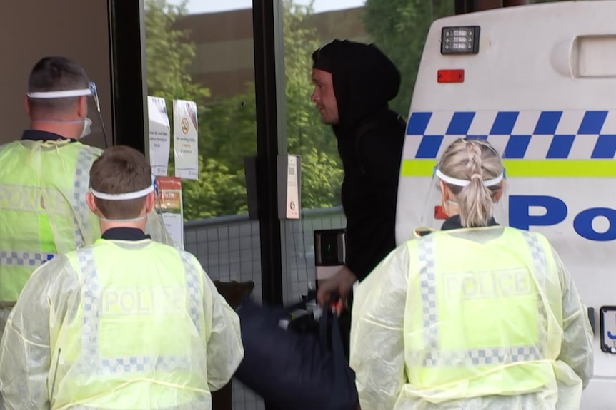 Hooded man surrounded by police in PPE.