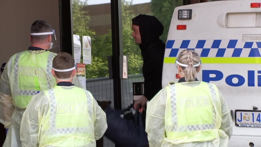 Hooded man surrounded by police in PPE.