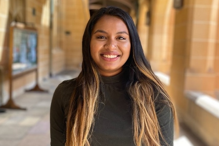 A woman smiles at the camera while standing under arched university hallways