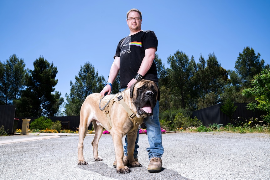 A man wearing a black T-shirt standing with a large brown dog.