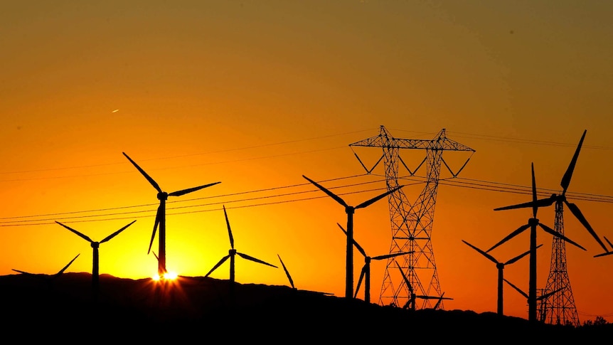 Wind turbines at sunrise with power lines in the background.