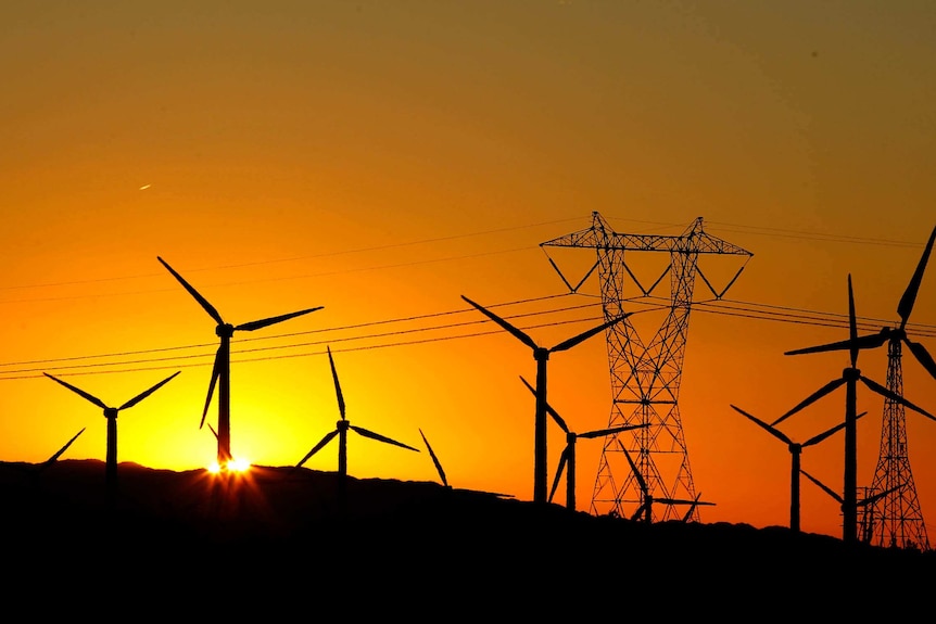 The sun rises behind a cluster of wind turbines.