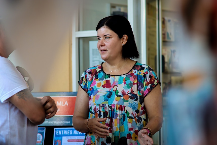 A woman wearing a bright dress is talking outside Nightcliff MLA stand.