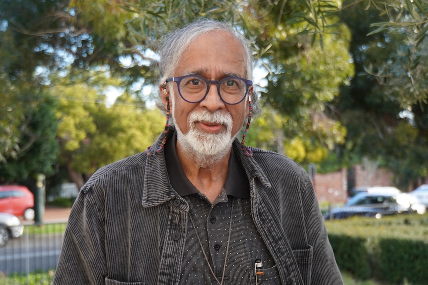A mid shot of Suresh Rajan posing for a photo outdoors wearing spectacles and a black shirt and jacket.