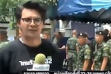 Soldiers are seen lining up in the background behind a reporter during a news broadcast