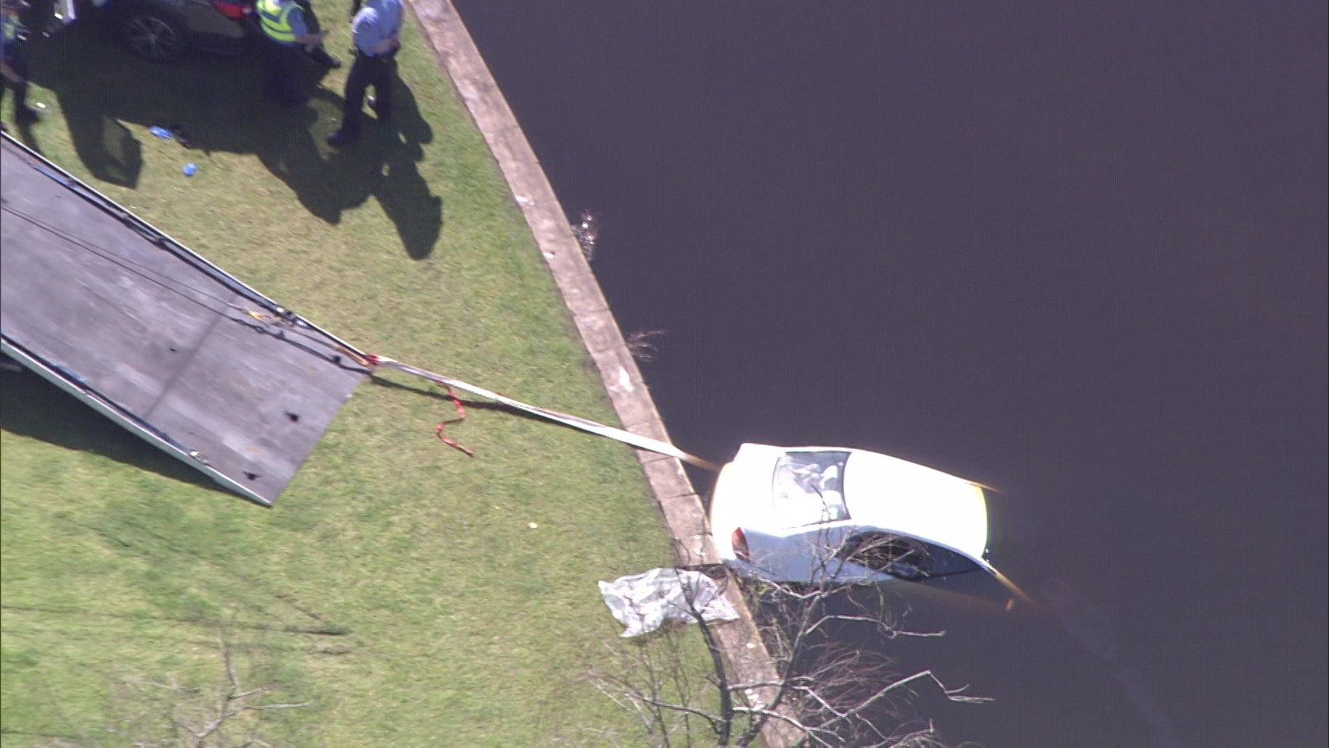 A car half submerged in a lake with a tow truck ramp next to it 