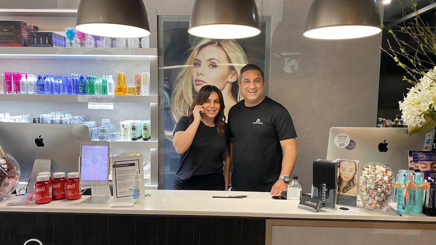 a woman and man standing behind a salon counter and smiling