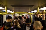 The inside of a busy Melbourne train with a lot of standing passengers.