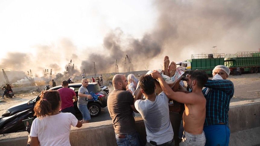 A group of men hold up a person to get them into a waiting car as smoke blows in the background.