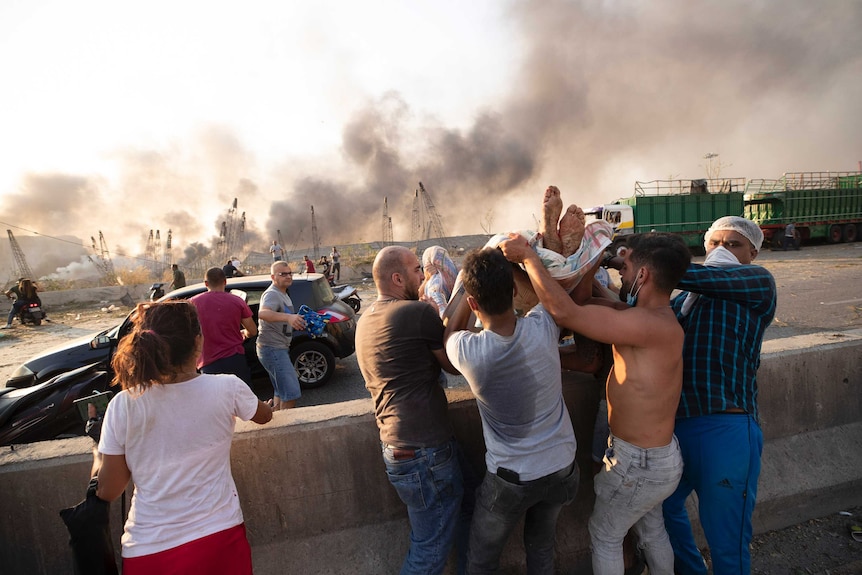 A group of men hold up a person to get them into a waiting car as smoke blows in the background.