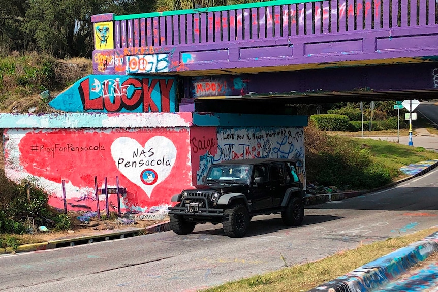 A jeep drives under a brightly painted bridge, painted with tributes to those killed