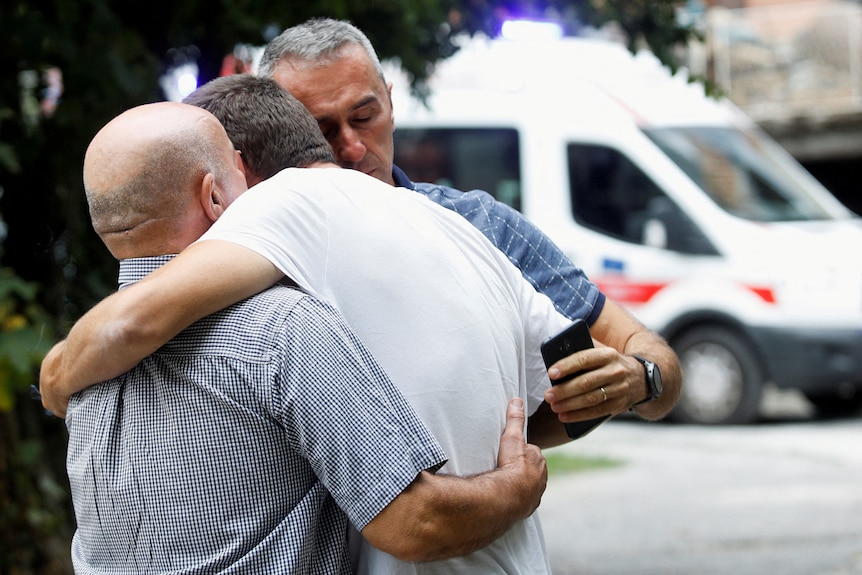 three men hug each other outside following a shooting in Montenegro