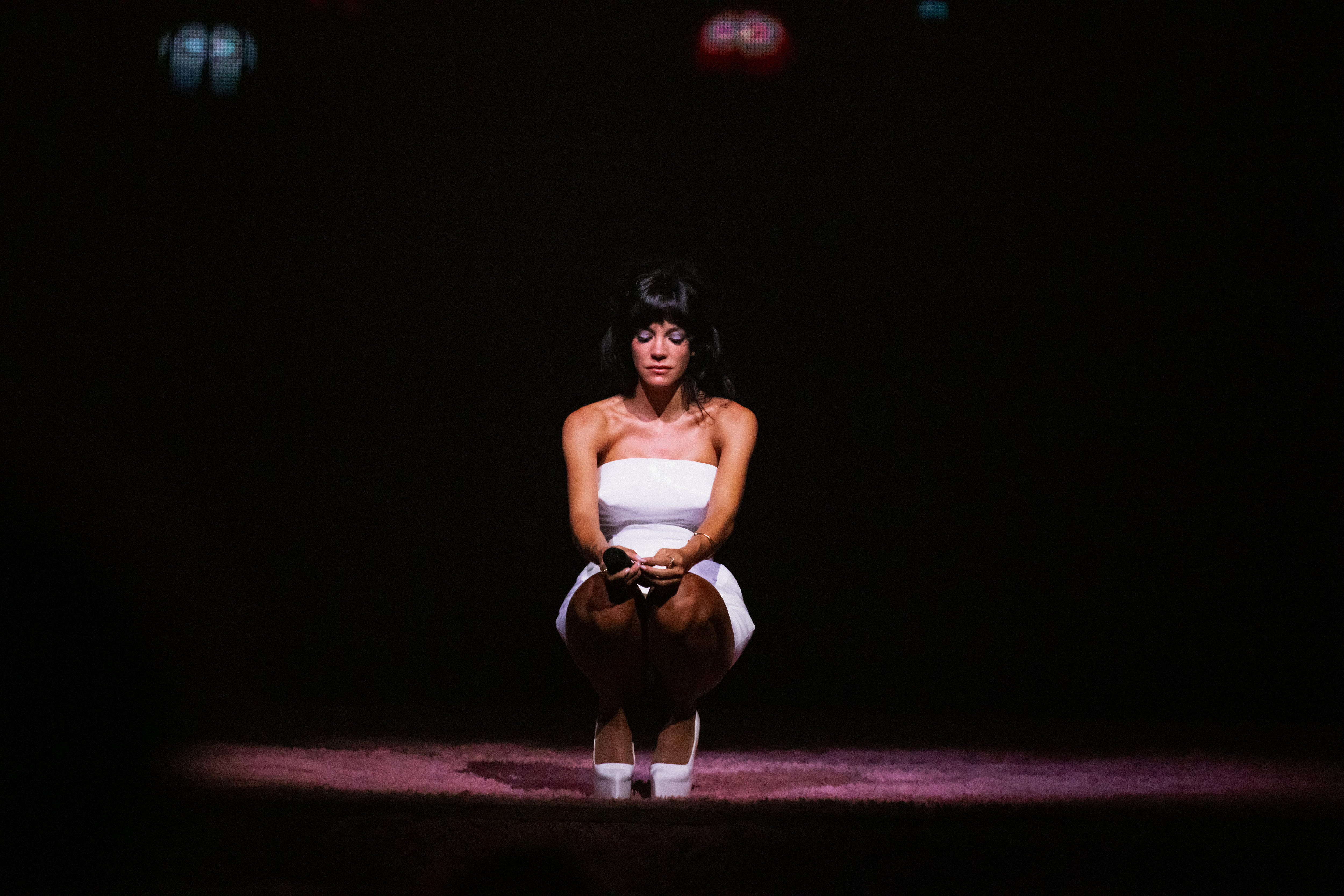 Allen, wearing a white mini dress, eyes down cast, kneels on the stage at TikTok Entertainment Centre.