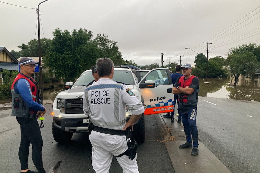 Several men standing on a road, in front of a white police car