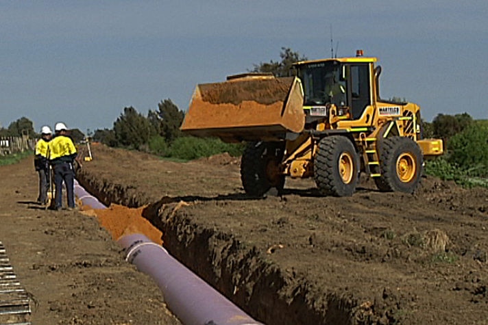 Workers in high vis and a tractor work alongside a long ditch in which a large pipe is being laid.