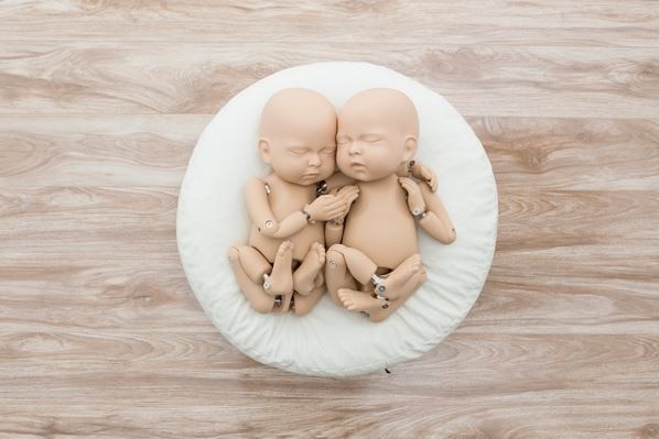 Two nude mannequin babies posed side by side on a circular white cushion.
