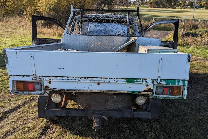 A ute abandoned in a grass field, with both driver and passenger doors open and green paint seen on the ute tray.