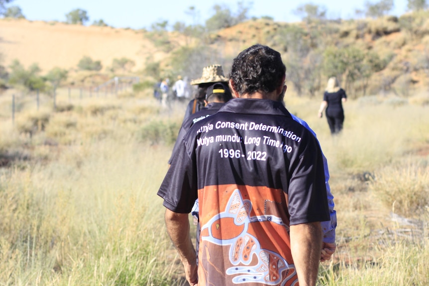 Group walks in Kunja Country where the back of a shirt reads 'Kunja Consent Determination 1996-2022'