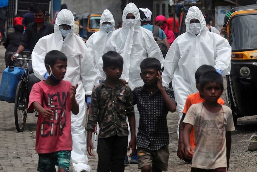 Health workers in protective gear walk behind a group of young boys.