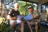 Rodney Pilling and Ray Bischoff sit on chairs and look at documents in front of a caravan at the park.