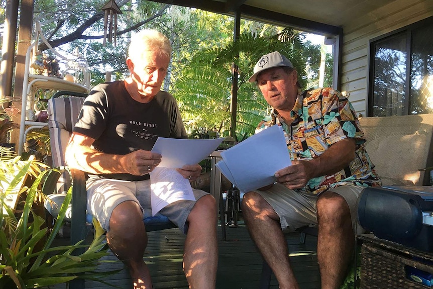 Rodney Pilling and Ray Bischoff sit on chairs and look at documents in front of a caravan at the park.