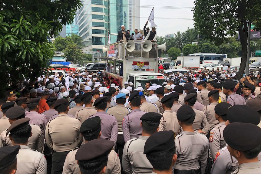 Huge crowd in street around van with loudspeakers and protesters on top.